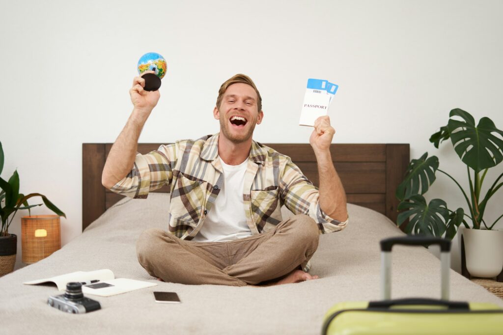 Portrait of cheerful, happy tourist, man sitting with plane tickets and a globe, packed suitcase